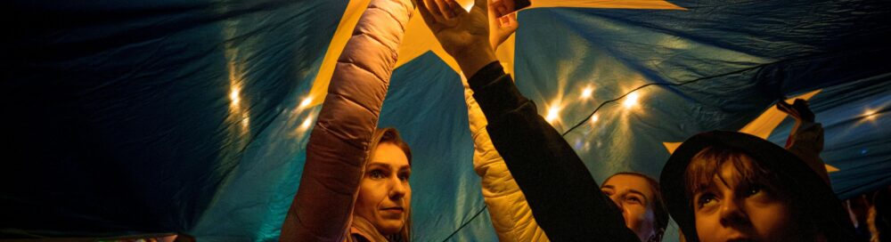Demonstrators shine the lights of their mobile phones as they stand under a large European Union flag, during a pro-EU rally ahead of the second round of the presidential election redo in Bucharest, Romania, Friday, May 9, 2025.