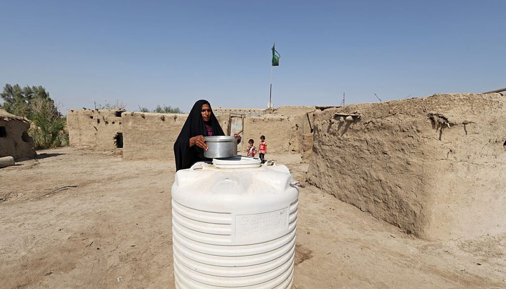 A woman collects water from a water tank stored outside her home in the village of Al-Bouzayyat, which sits on the bank of a former canal which has dried up, in Diwaniya, Iraq, October 11, 2022.