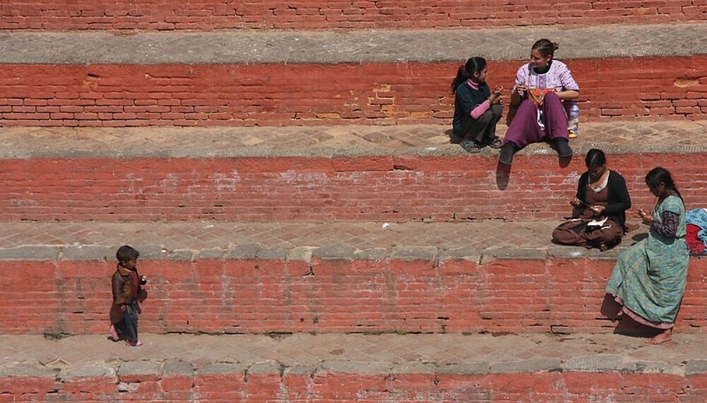 Picture of a groups of Nepalese people sitting on a set of stairs made out of brick.